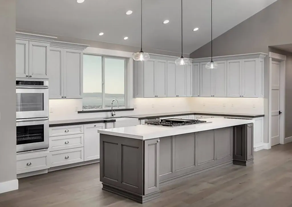 What professional cabinet refinishing involves — freshly finished white kitchen cabinets with gray island and modern pendant lighting