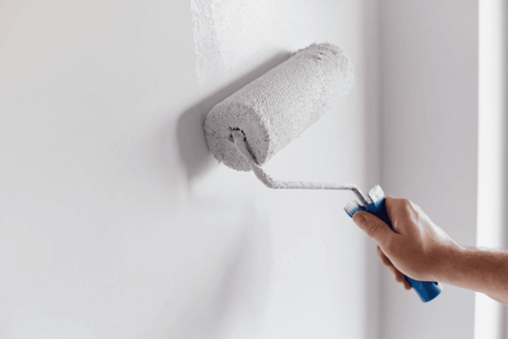 What paint sheen means for interior painting — painter rolling gray paint onto a smooth interior wall